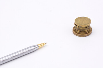 Silver pen on a stack of coins on a white background. Business Concept
