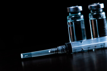 2 doses of Sars-Kov-2 coronavirus vaccine in transparent glass ampoules, covered with frost and a disposable syringe, on a dark background, short focus, toning