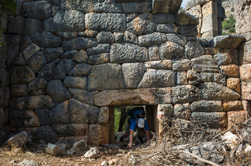 Hiking Lycian way. Man is trekking through low doorway of Pydnai Ruins, well-preserved polygonal...
