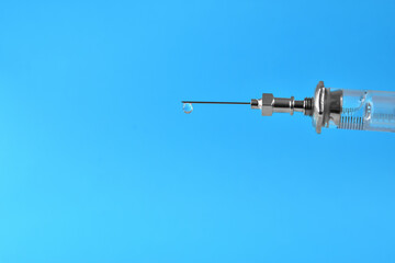 syringe with a drop of medication at the end of the needle on a blue background. Medicine injection.