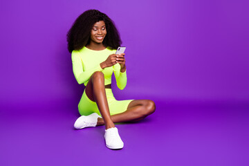 Photo of charming girl hold telephone look screen wear green shirt shorts sneakers isolated violet background