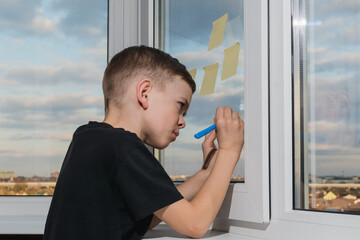 A little boy writes on a sticker stuck to the window