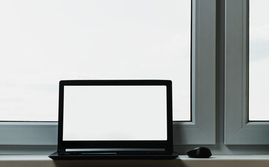 A black laptop for work stands near the window