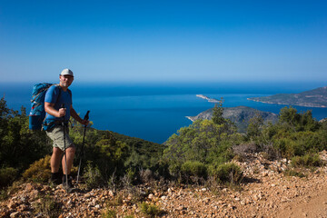 Fototapeta na wymiar Hiking Lycian way. Man tourist is standing on path over Mediterranean sea coast on Lycian Way trail on stretch between Kalkan and Kas, Trekking in Turkey, outdoor activity
