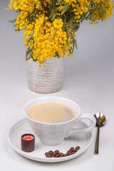 A cap of coffe with sweet and coffee beans near the vase with flowers