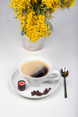 A cap of coffe with sweet and coffee beans near the vase with flowers
