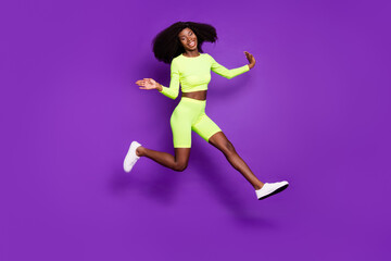 Photo of cheerful active lady jump run have fun wear green shirt shorts footwear isolated violet background