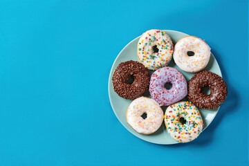 Mmm, so delicious. Top view of various colourful round glazed donuts with sprinkles on the plate over blue background