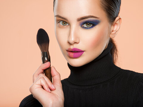 Portrait of a girl with cosmetic brush near face. Woman making makeup on the face using makeup brush. One half face of a beautiful white woman with  bright makeup and the other is natural.