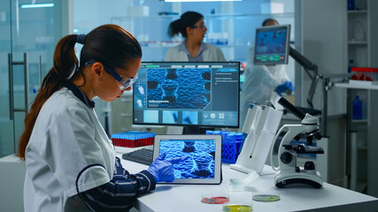 Lab technician doctor analyzing virus evolution looking on digital tablet. Team of scientists...