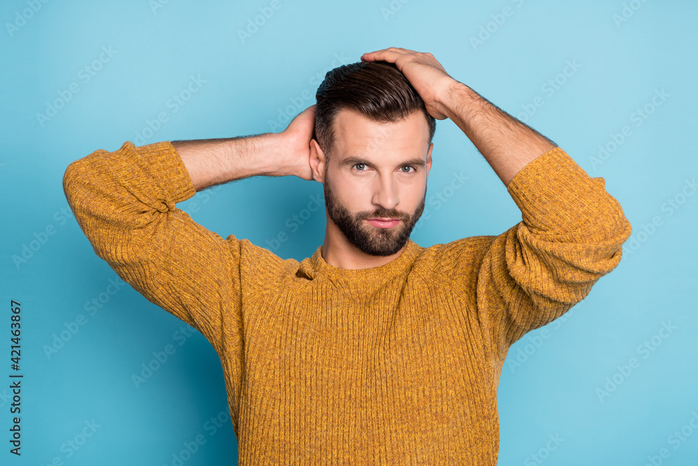 Wall mural Photo of young confident serious handsome cool man fixing hairstyle wear yellow knitted sweater isolated on blue color background