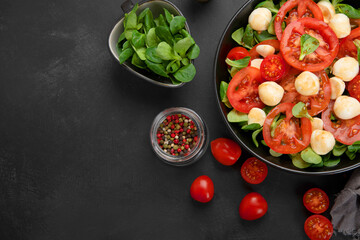 Delicious Italian caprese salad with sliced tomatoes and mozzarela on dark background.