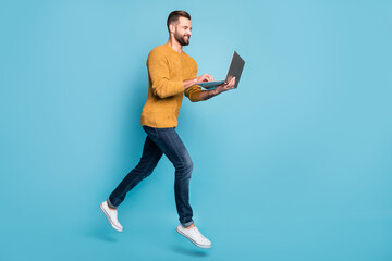 Full length body size view of nice cheerful skilled focused guy jumping going using laptop isolated over bright blue color background