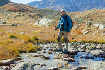Obraz premium Hipster mountain blogger for lifestyle design. Adventure tourism. Trekking of young man vlogger with camera. Solo tourist in the Alps. hoto with copy space