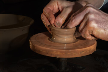Potter at work. Potter's hands in clay form a pot on a circle. Light hands on dark background