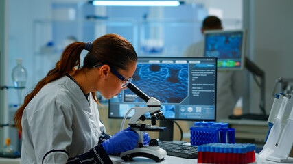 Scientist looking at biological samples under microscope typing on pc. Team of chemists working in lab, examining virus evolution using high tech for scientific research of vaccine development.