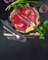 Meat raw steaks with seasoning and herbs on dark background.