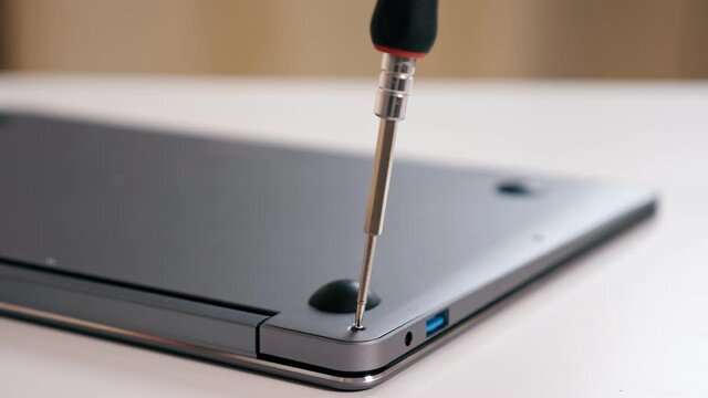 Close-up of screwing bolts with screwdriver on silver laptop.