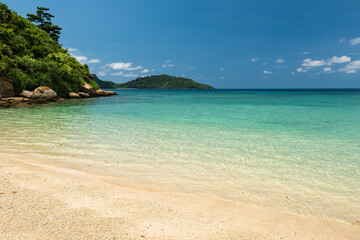 Beautiful landscape of peaceful beach, with vegetation on rocks, island in the background, calm emerald green sea and perfect for relaxing.