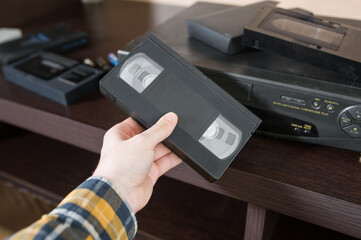 A man's hand in a checkered yellow shirt inserts an old tape cassette into a video player