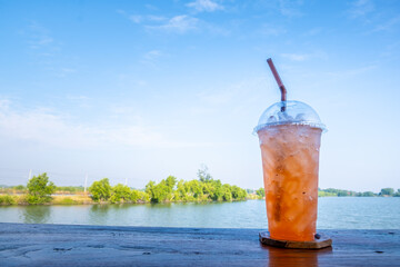 Close up iced plum liqueur soda in plastic glass on wooden table with blue sky background.