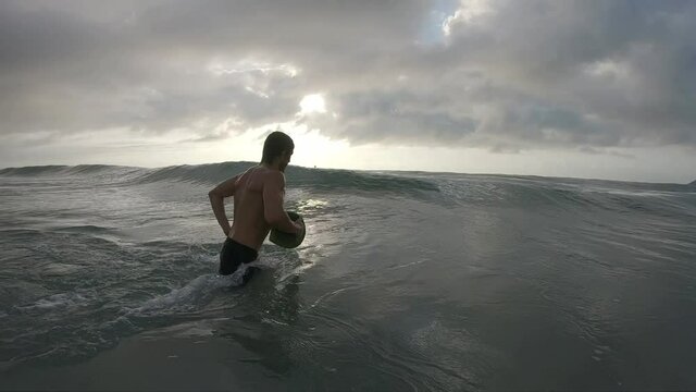 Sunrise bodyboarding. Young man with handplane passes coming ocean wave at sunrise
