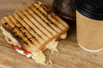 big sandwich with ham, cheese, tomatoes and disposable coffee cup on toasted bread