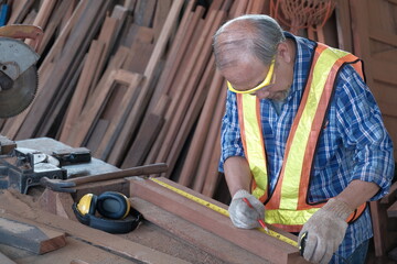Old Asian man carpenter working in a woodworking factory. They are using a tape measure and a...