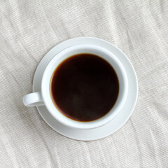 black coffee in a cup with a saucer on a tablecloth top view. regular hot everyday drink
