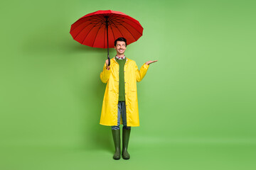 Full length body size view of attractive cheerful guy wearing raincoat checking rain drop isolated over bright green color background