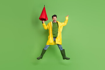 Full size photo of young excited man happy positive smile jump up hold umbrella wear raincoat...