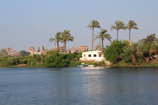 A small white house in the middle of green trees with a boat in front of it in the water in Rashid in Egypt