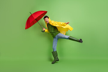 Full size profile photo of brunet optimistic guy fly with umbrella wear cloak boots isolated on green color background © deagreez