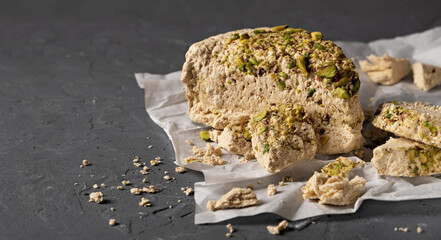 Walnut halva with pistachios lies on parchment paper on a gray textured background. Traditional oriental dessert.