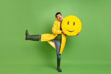 Full length photo of young cheerful man happy positive smile hold paper pinata emoji wear raincoat...