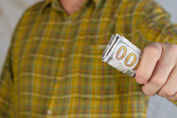 An adult man in a green-and-yellow plaid shirt passes the money to the camera.