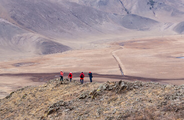 Tourists wearing red and blue clothes having rest on the top of mountain. Mountain valley landscape.