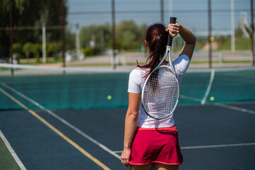 Woman in skirt standing back on the tennis court and holds the racket.