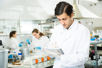 Student of Faculty of Biology performing experiments in university laboratory, writing results in workbook..