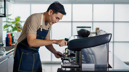 Asian short black hair young successful handsome male barista wearing brown shirt and dark blue jeans bib apron stand smiling use high technology luxury coffee maker machine in coffee shop restaurant