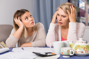 Sad mother and her adult daughter with big financial problems are sitting at home