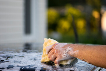 washing the car roof with a microfiber cloth. car wash. water, foam, shampoo. car roof and hand with a washcloth. washes the metallic black surface