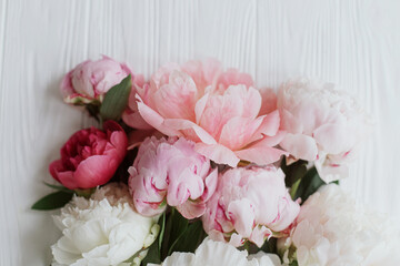 Beautiful tender peony bouquet flat lay on white wood. Happy Mothers day.  Floral greeting card