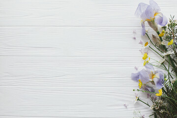 Beautiful iris flowers, daisy and yellow wildflowers border on white wood, flat lay with copy space
