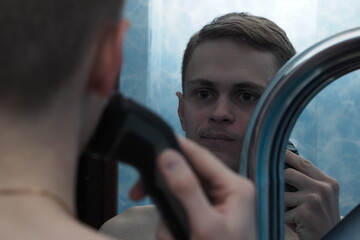 A young man of European appearance shaves his face with