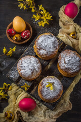 Obraz na płótnie Canvas Traditional Easter buns with colored eggs and yellow flowers on a dark background. Vertical arrangement