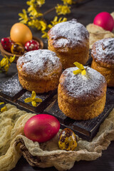 Traditional Easter buns with colored eggs and yellow flowers on a dark background. Close-up, background in soft blur. Vertical arrangement