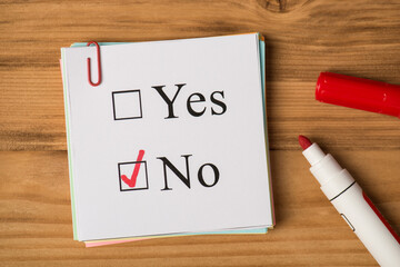 Top view photo of card filling form with answer no and red marker on wooden table background