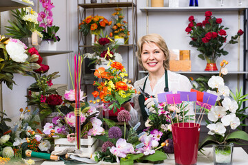 Pleasant female florist wearing an apron and happily preparing flowers in floral shop