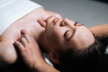 Fototapeta na wymiar Close-up top view of young woman lying down on massage table with closed eyes during shoulder and neck massage at spa salon. Male masseur professionally massaging shoulders on black background.